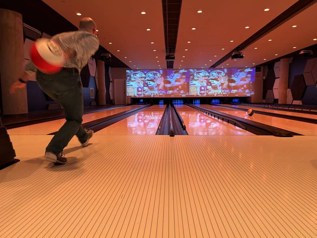 In an empty but inviting bowling alley, a bowler reaches back with his bowling ball for a backswing just before releasing it down the lane.