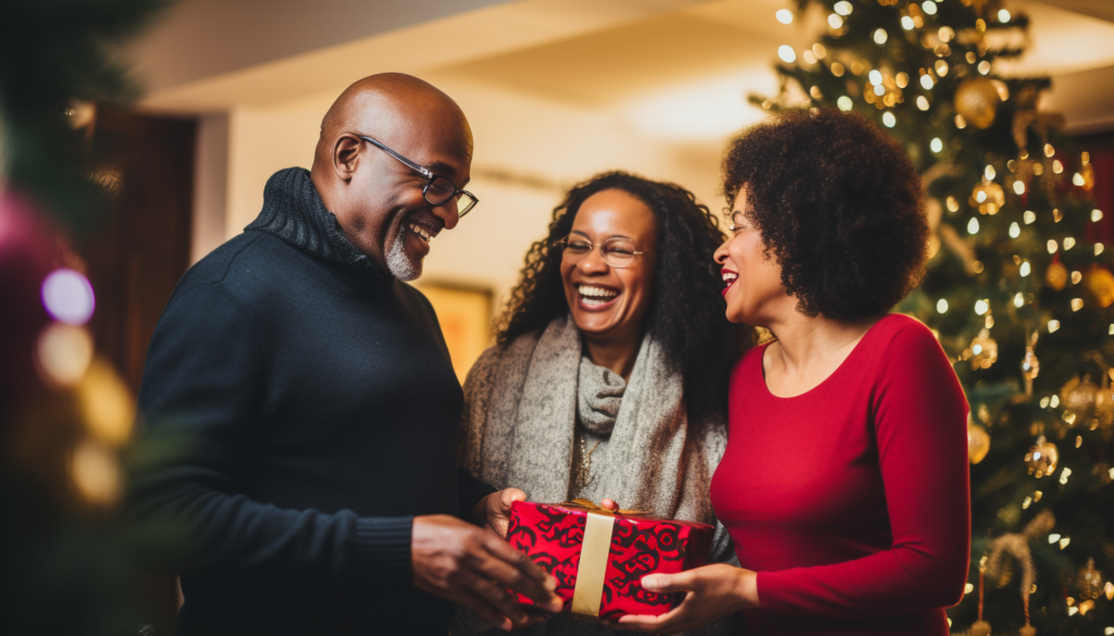 A man and two women exchange a festive red gift in front of a Christmas tree.